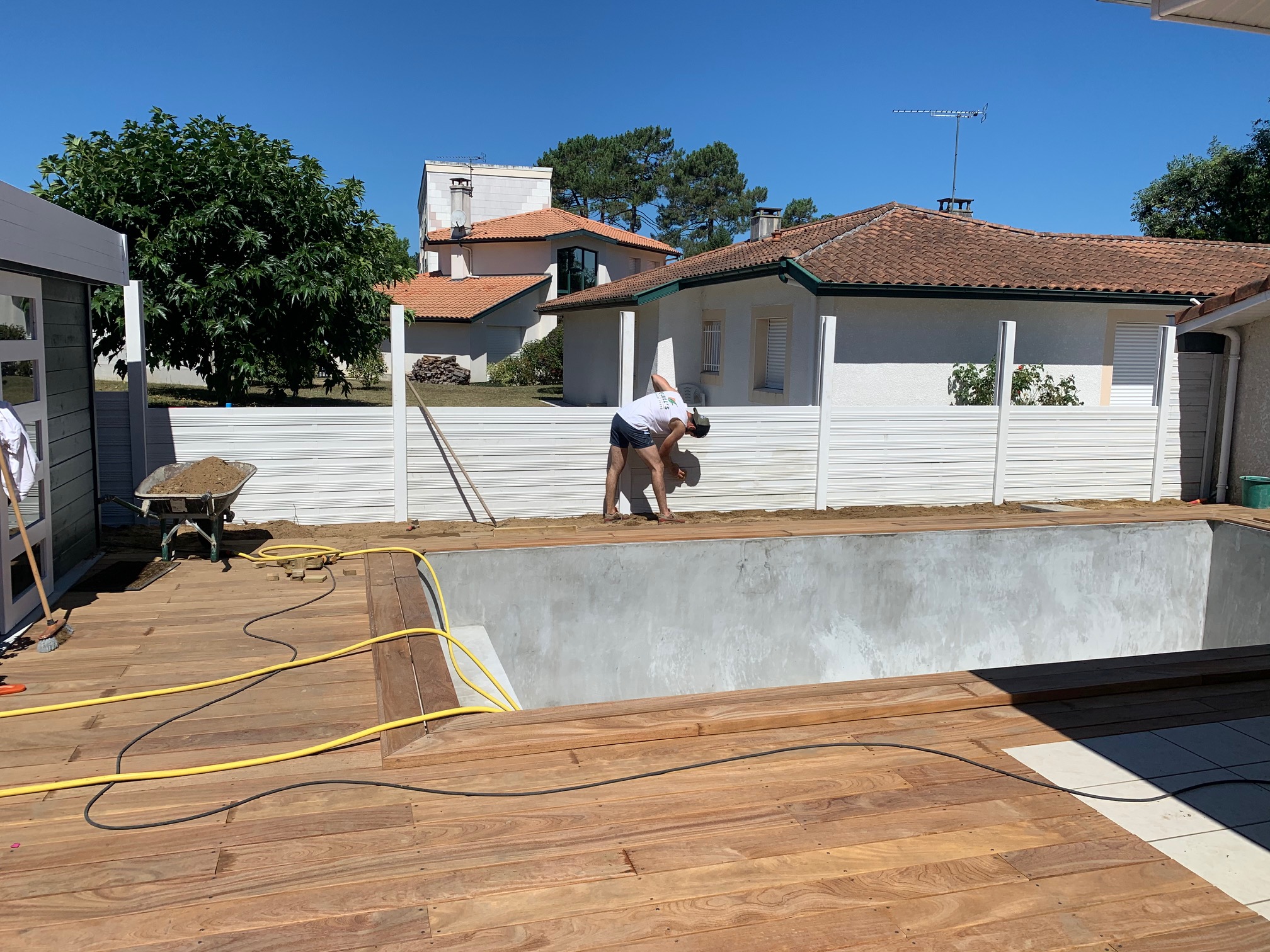 Homme relaxé près d'un olivier bonsaï dans son jardin Un homme souriant en t-shirt vert et short beige assis à côté d'un olivier bonsaï dans un jardin aménagé.