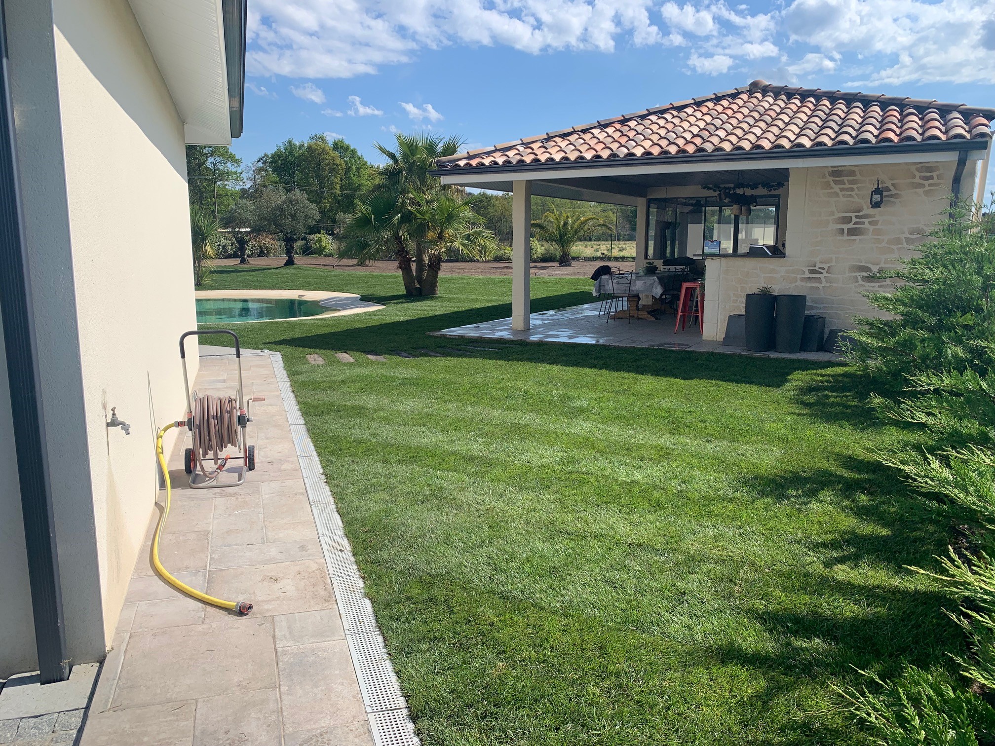 Homme relaxé près d'un olivier bonsaï dans son jardin Un homme souriant en t-shirt vert et short beige assis à côté d'un olivier bonsaï dans un jardin aménagé.