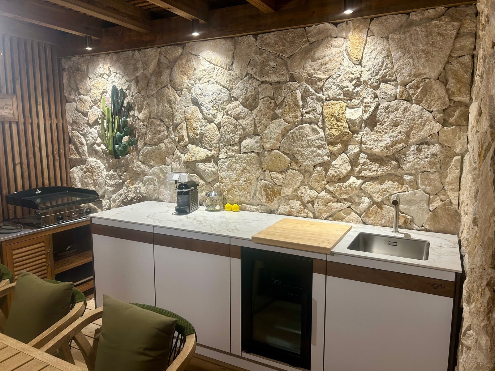 Cuisine d'été moderne avec mur en pierre naturelle, plan de travail blanc, évier et frigo à vin intégré.